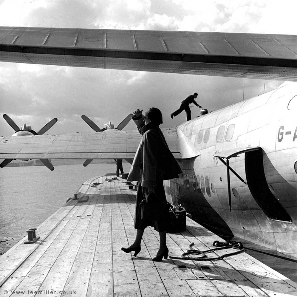 Fashion model standing next to flying boat in Augusta Harbour, Sicily